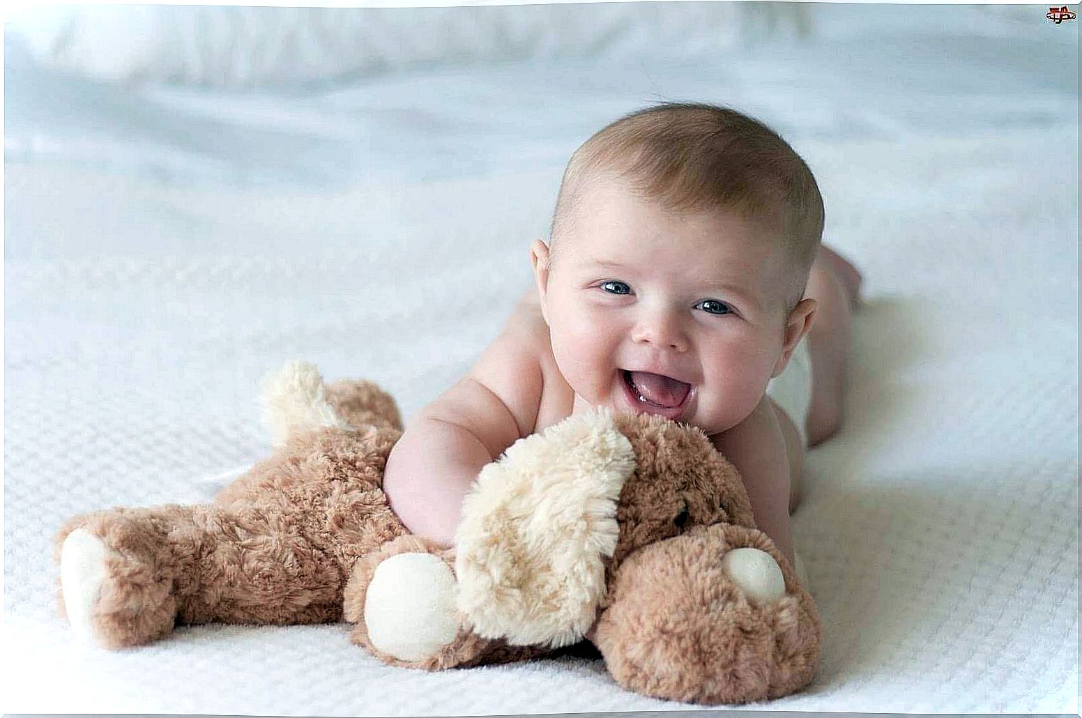 Christening gift ideas: Baby laughs with teddy bear.