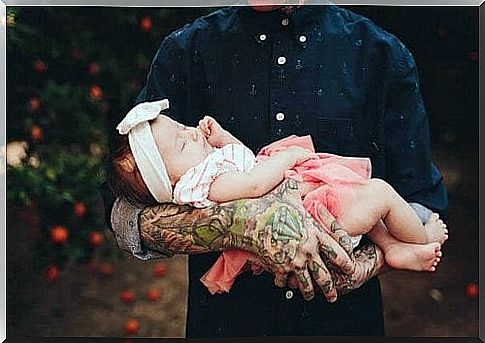 little baby lying in tattooed arms