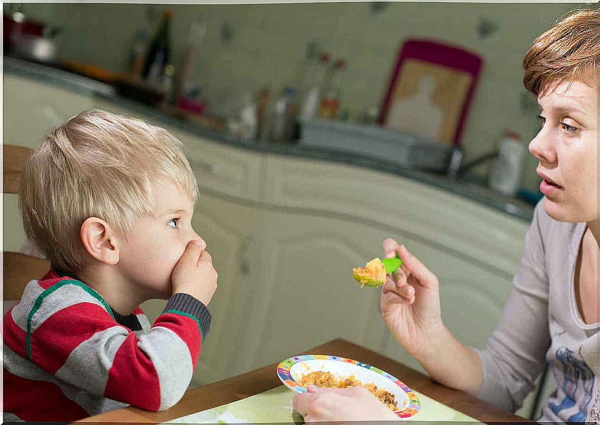 A small child covers his mouth while his mother tries to feed him