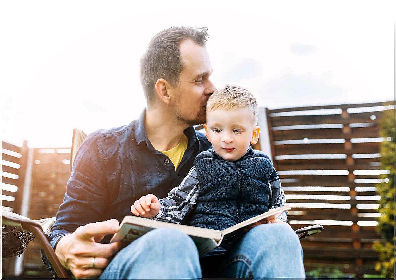 A father reading a book outdoors with his son on his lap