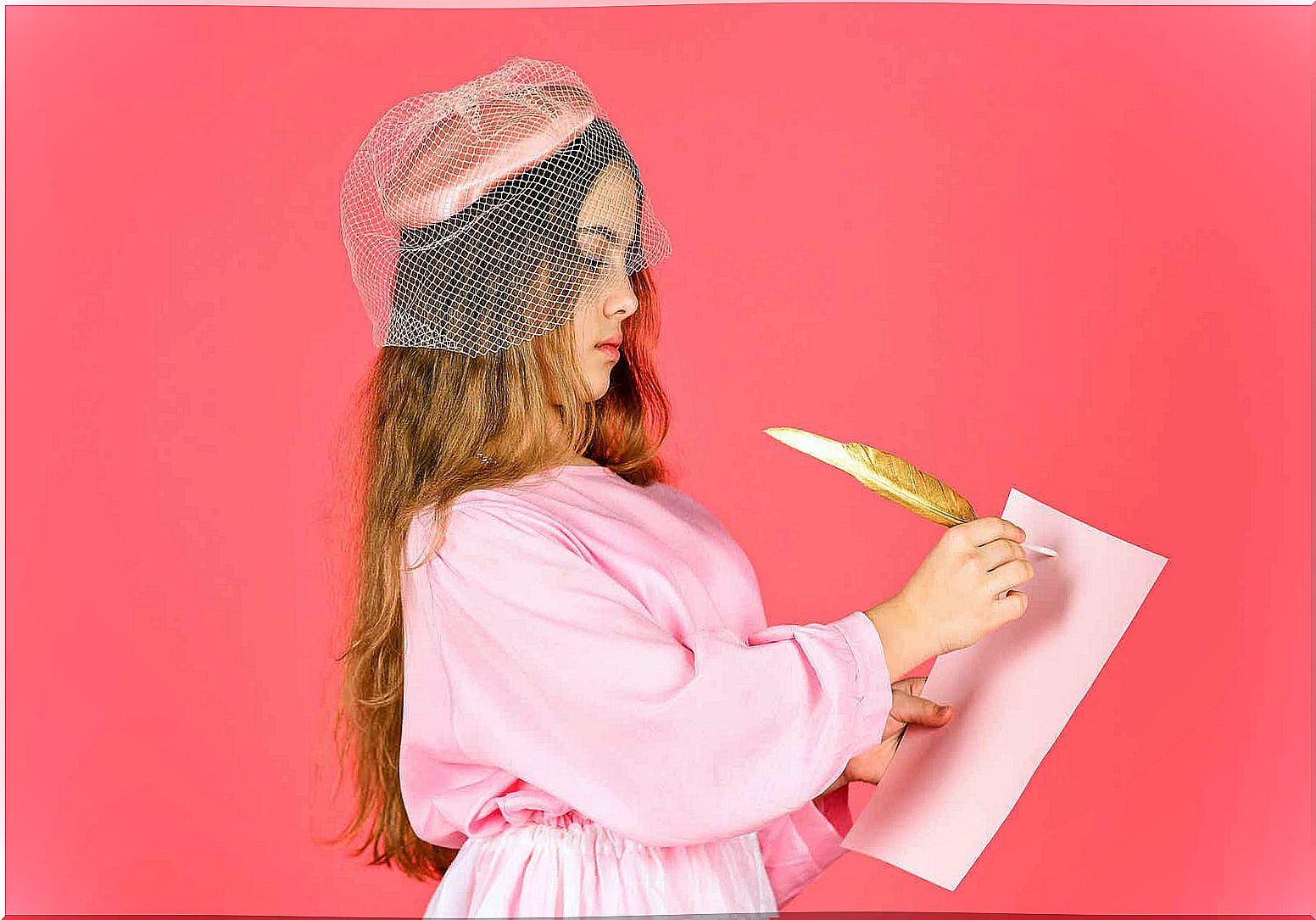 A girl dressed in an old-fashioned hat and dress, writing on a piece of paper with a feather