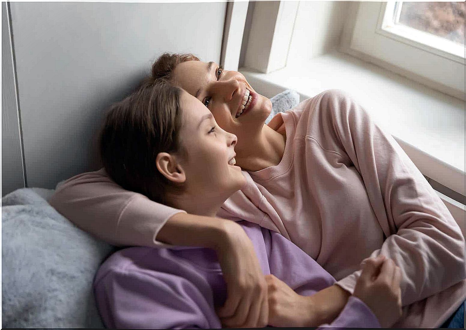 A mother and daughter are lying on the couch smiling