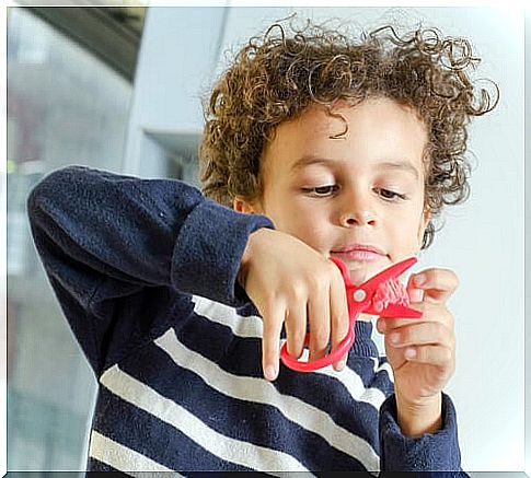 little boy cutting with a pair of red scissors