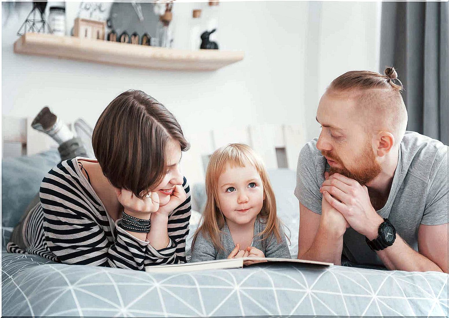 Parents and daughter lying in bed reading a book