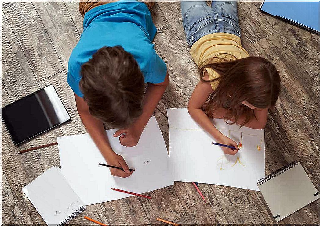 A boy and a girl lying on the floor drawing