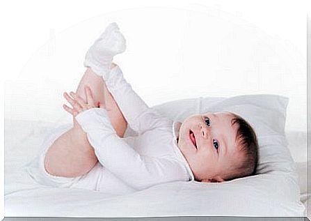 happy baby lying in bed and peeling at his toes